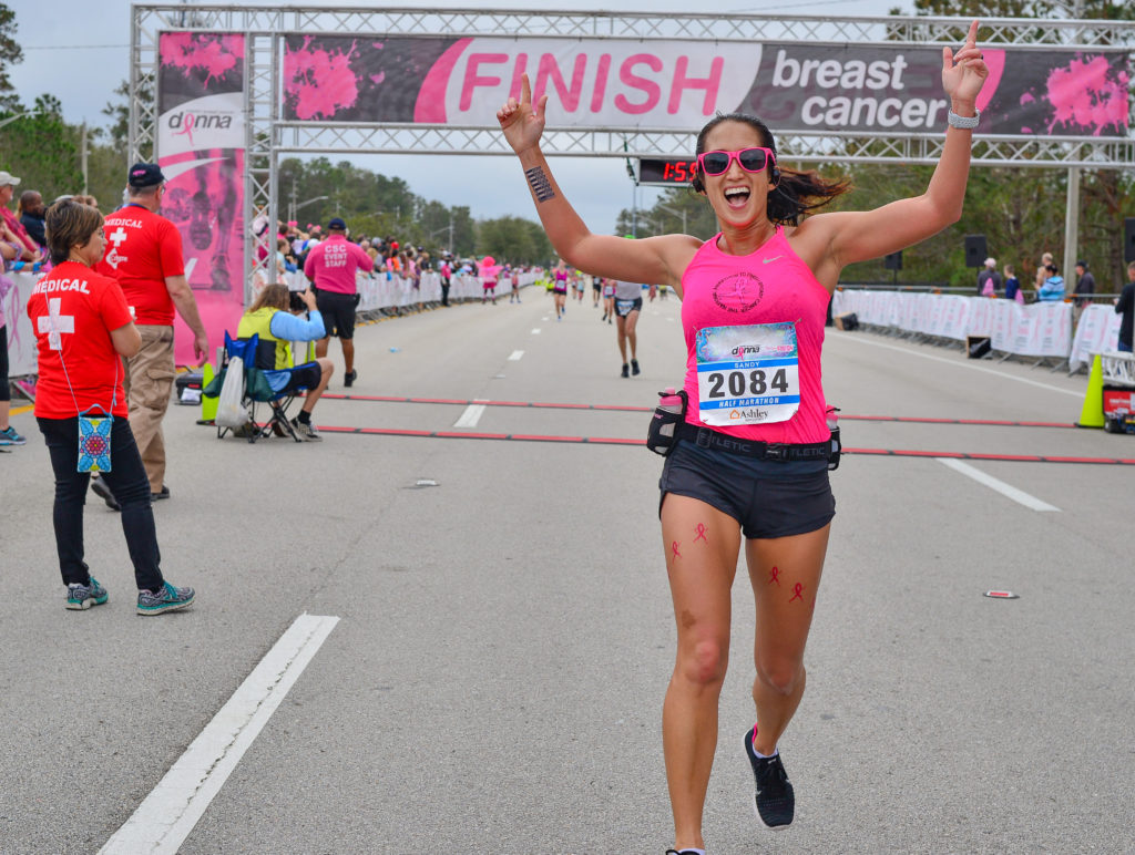 A woman crossing the finish line of a race with her arms raised high