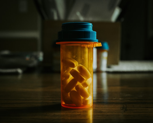 Prescription pill bottle with yellow pills inside, on a wooden surface.